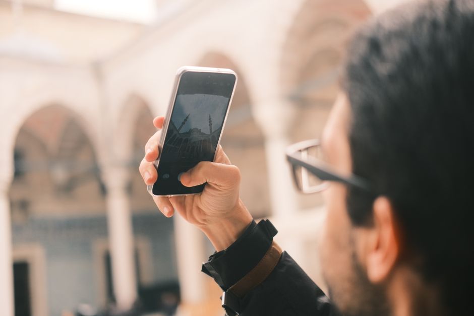 Marketing Turístico — An adult male photographs a mosque using a smartphone outdoors with a focus on capturing architecture.