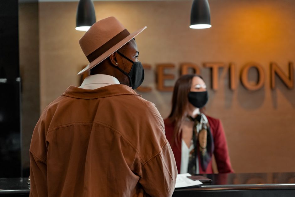 Marketing Turístico — Man in mask at hotel reception during pandemic, interacting with masked receptionist.